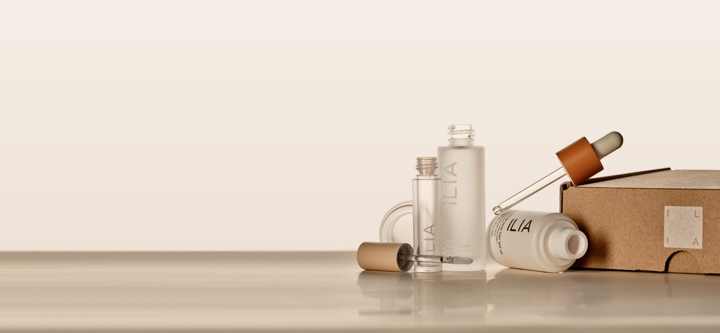 Minimalist, empty beauty products with ILIA branding, including serum and mascara, placed on a neutral surface.